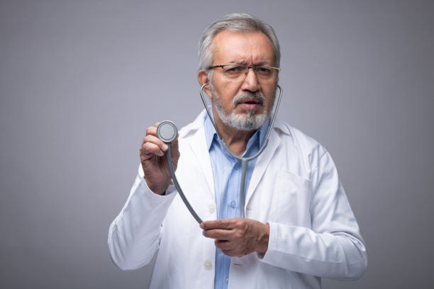 成熟的医生穿着白色制服，背景为灰色的库存照片图片下载