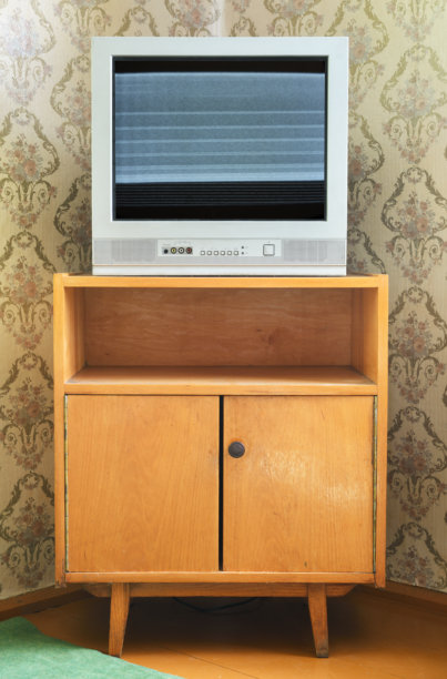 一台旧电视机放在床头柜上，背景是壁纸的图案。图片下载