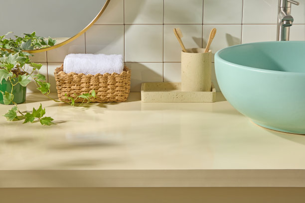 编织篮子里放着白色毛巾、绿色洗脸盆和竹制牙刷，放在米色台面上。明亮的自然光和瓷砖墙面营造出一个柔和、简约的浴室场景，空间清晰。图片下载