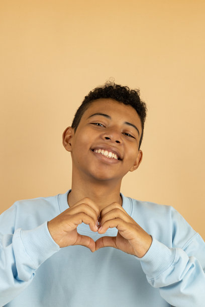 一位快乐的棕肤青少年在浅棕色背景上用双手做出心形手势的竖版图片图片下载