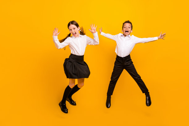 穿着白衬衫的有趣幸运的学龄前儿童在黄色背景下高高跳起的全身照片图片下载