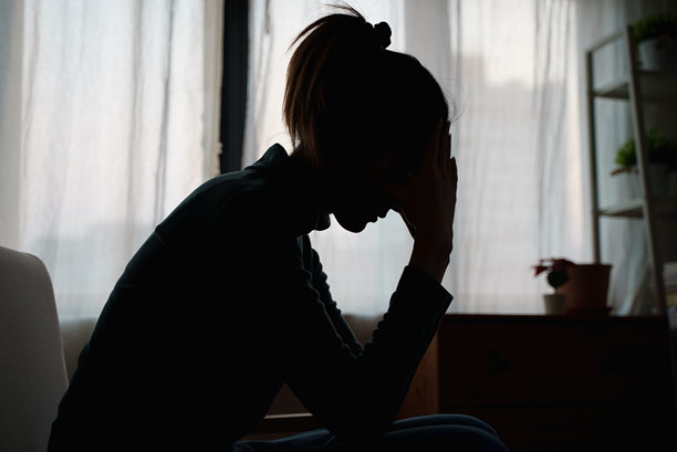 年轻的亚洲女子独自坐在卧室里的剪影照片，感觉不好和不开心，同时思考她的问题，代表失败，失去的爱，抑郁。阴暗、喜怒无常、消极的情绪。图片下载