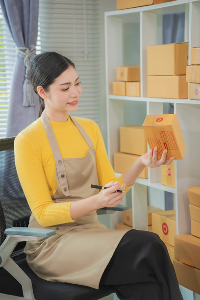 亚洲女性送货概念，自由职业者，网上购物，家中使用笔记本电脑与包裹箱，在线中小企业，竖版照片。图片下载