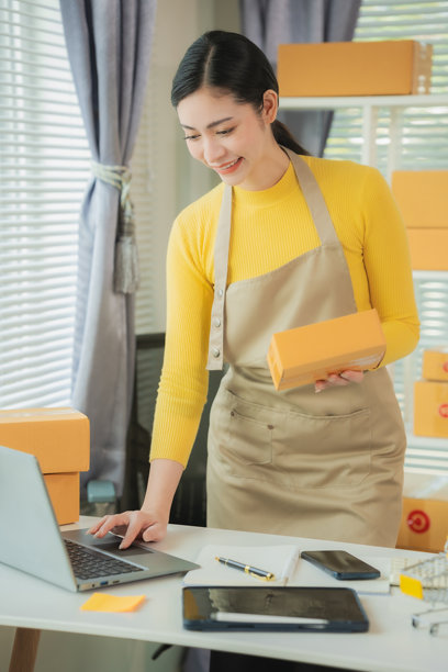 亚洲女性送货概念，自由职业者，网上购物，家中使用笔记本电脑与包裹箱，在线中小企业，竖版照片。图片下载