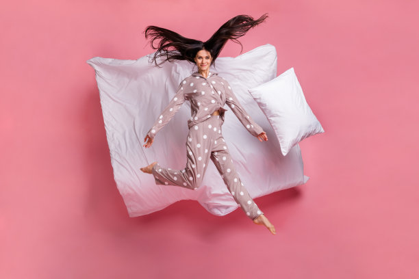 可爱的迷人年轻女士穿着睡衣在粉色背景上高高跳起的全身照片图片下载