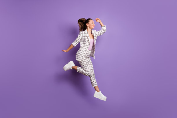 年轻女孩的全身侧面照片，开心积极，微笑着向前看，跳起，背景为紫色。图片下载