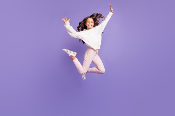 年轻疯狂女孩在紫色背景上跳跃于蹦床，享受快乐时光，满脸笑容的全身照片图片下载