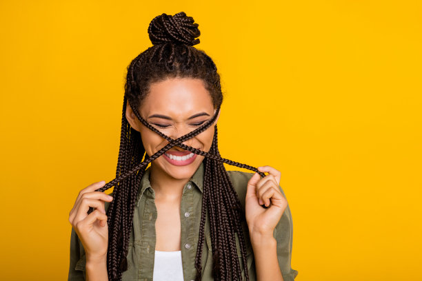 可爱女孩的照片肖像，脸上有两缕交叉的头发，微笑着，背景为鲜艳的黄色。图片下载