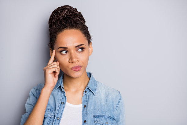 惊讶女孩的照片肖像，扎着发髻，沉思着做决定，目光投向空白处，背景为灰色。图片下载