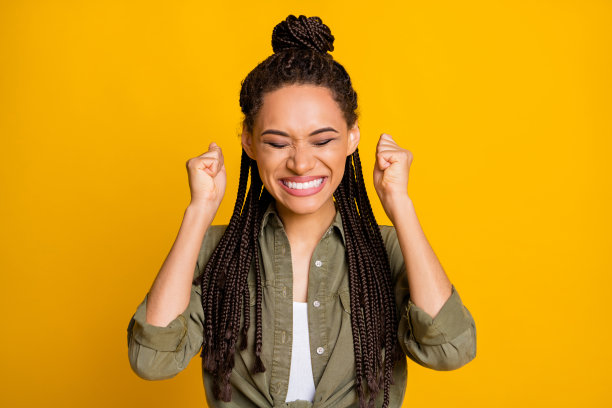 女孩在鲜艳的黄色背景下庆祝，双手举起拳头的照片肖像图片下载