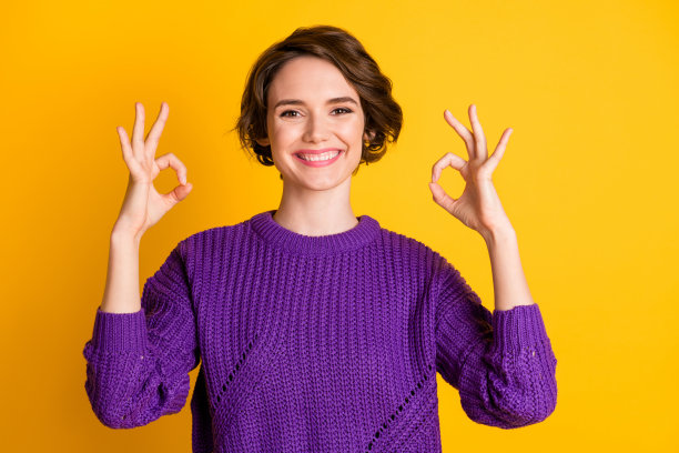 快乐女孩在鲜艳的黄色背景下做出两个“OK”手势的照片肖像图片下载