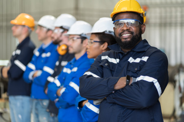 工业工厂。穿着安全制服和安全帽的男性工程师肖像，双臂交叉站在工厂里。男性工程师团队的半身照片，面带微笑，快乐的样子。图片下载