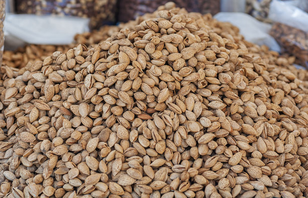 一堆丰盛的生杏仁连壳特写，拍摄于户外市场摊位，采用选择性对焦。这张生动自然的照片突显了丰富的质感和新鲜的丰盈，非常适合健康饮食和市场农产品的主题。图片下载