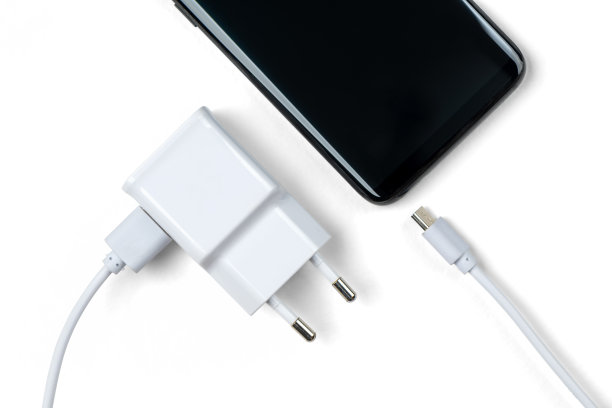 白色智能手机充电器，配有USB数据线和现代黑色手机。背景为白色，带有抠图路径。干净简约的科技设备图片。图片下载