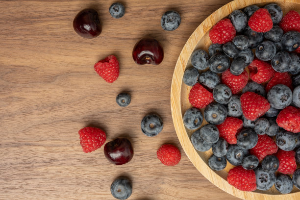 高分辨率的混合水果照片，包括樱桃、覆盆子和蓝莓，摆放在盘子上，采用了分离焦点技术拍摄。图片下载