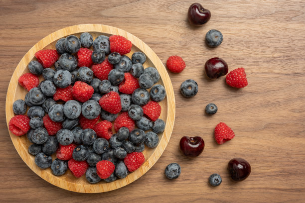 高分辨率的混合水果照片，包括樱桃、覆盆子和蓝莓，摆放在盘子上，采用了分离焦点技术拍摄。图片下载