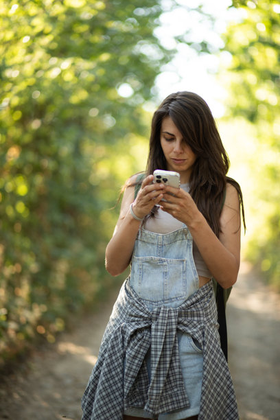 年轻的徒步旅行者在阳光明媚的森林小径上使用智能手机。库存照片图片下载