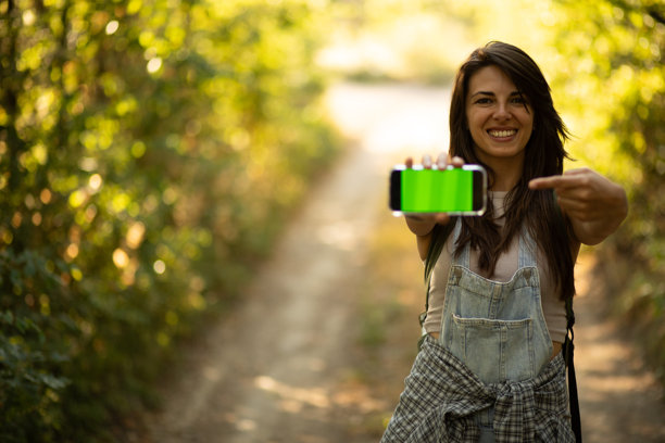 年轻的徒步旅行者在树林中展示带有绿色屏幕的智能手机。库存照片图片下载