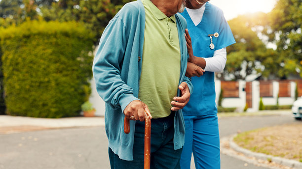 护士和一位使用拐杖的老人在户外相互扶持，帮助走路，进行康复或伤后恢复。照顾者帮助有残疾的患者保持平衡，并引导其进行退休后的康复。图片下载