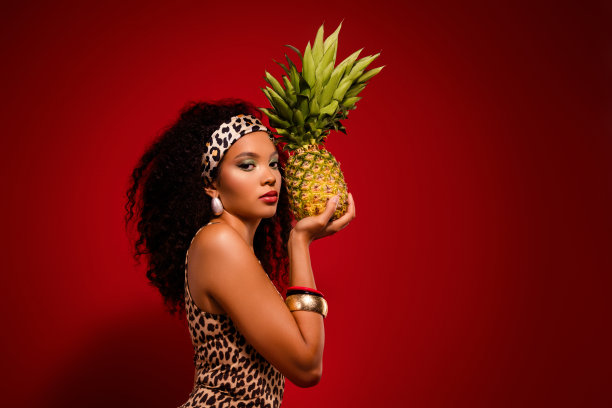 优雅的女性模特穿着豹纹服装，手持菠萝，背景为充满异国风情和魅力的鲜艳红色。图片下载