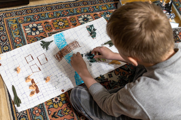 孩子专注于在手绘纸地图上摆放玩具士兵，策划地板上的战略玩具战斗场景图片下载