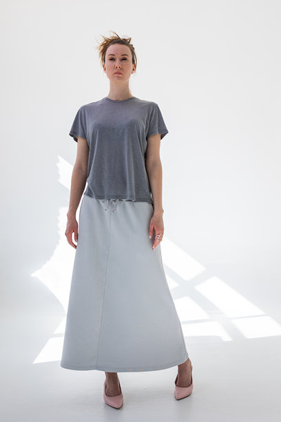 穿着灰色裙子和T恤的美丽女性，背景为白色。时尚女性风格。摄影棚拍摄。竖版照片。图片下载