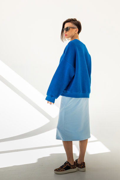 穿着蓝色卫衣和浅蓝色裙子的优雅女性，背景为白色。时尚女性风格。摄影棚拍摄。竖版照片。图片下载