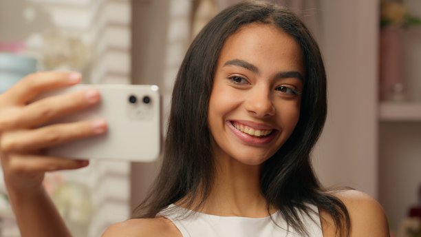 微笑的快乐拉丁裔女孩，西班牙裔女性时尚博主，影响者，模特，在浴室里拿着手机，美容博客，护肤品，化妆教程，社交媒体内容，自拍，视频通话。图片下载