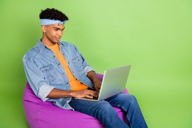 在鲜艳的绿色背景下，英俊的男士正在使用笔记本电脑进行项目工作的照片肖像，留有空白空间。图片下载