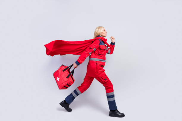 全身侧面照片，勇敢严肃的老年女急救员走路时手持包，穿着斗篷，背景为灰色。图片下载