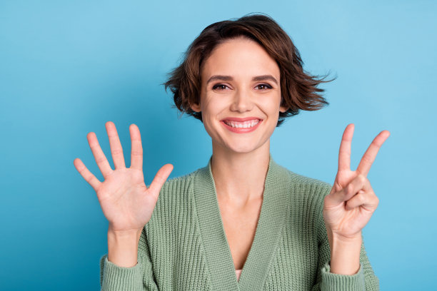 穿着绿色开衫的搞怪有趣年轻女孩在蓝色背景下数七根手指的照片图片下载