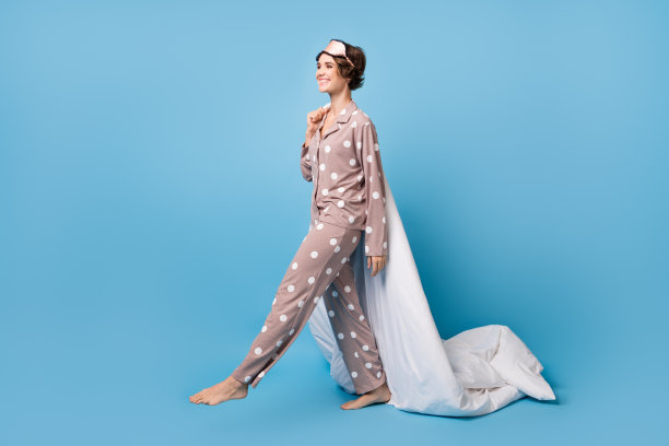 年轻女孩的全身侧面照片，兴奋快乐，微笑着抱着被子，准备入睡，背景为蓝色。图片下载