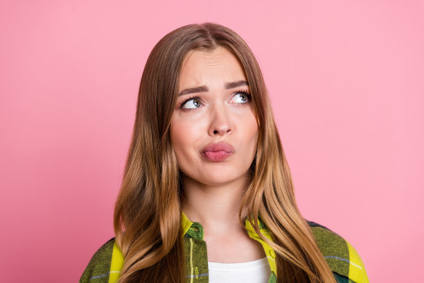 穿着黄色格子衣服的漂亮年轻女孩的照片肖像，表情怀疑和不满，背景为粉色，空旷的空间。图片下载