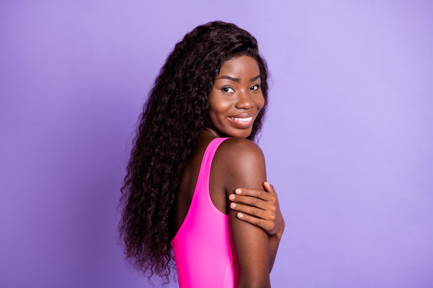 非洲裔美国女性在粉色背景下触摸肩膀，回头看着的肖像照片图片下载