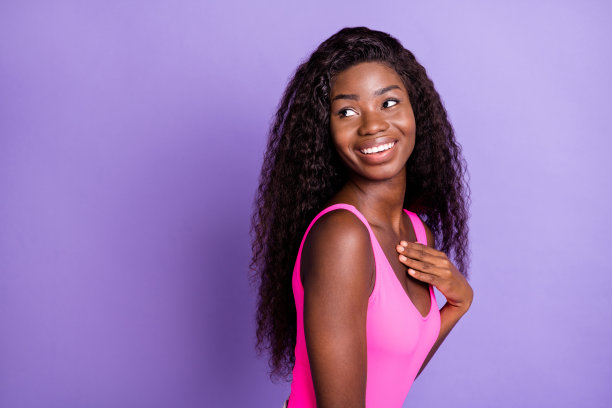 非洲裔美国女性的照片肖像，手触胸部，目光投向身后空白处，背景为柔和的粉色。图片下载