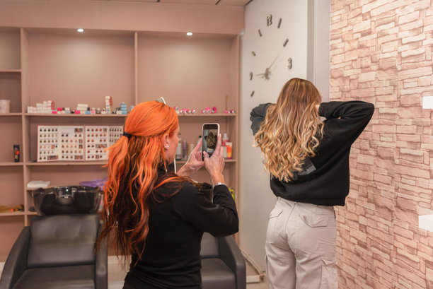 女发型师用智能手机拍摄客户在美容程序后卷发造型的照片。图片下载