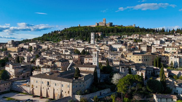 翁布里亚地区历史悠久的阿西西小镇的鸟瞰图，山顶上有马焦雷城堡，中世纪石建筑和绿色起伏的山丘，文化遗产和旅游照片内容。图片下载