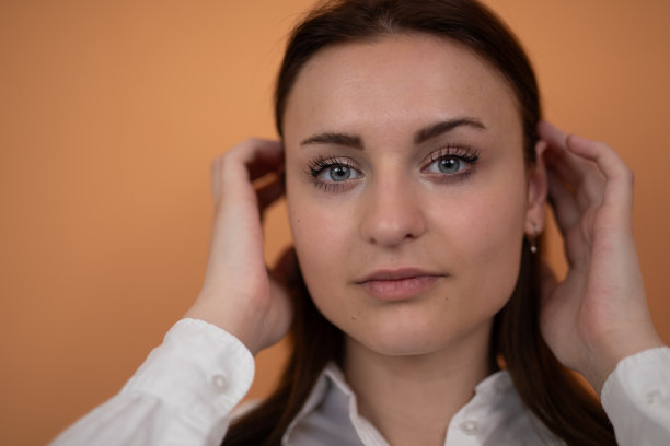 年轻女性在橙色背景下触摸头发并看向镜头。库存图片图片下载