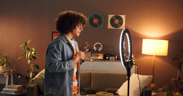在家中使用环形灯的男性时尚博主进行介绍，进行晚间直播和社交媒体活动。夜晚，内容创作者为观众评测服装，录制视频并提供搭配建议。图片下载