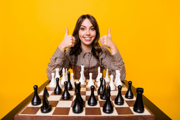 棕发女性在明亮的黄色背景上与棋盘上的白色棋子玩耍，做出点赞手势的照片肖像图片下载