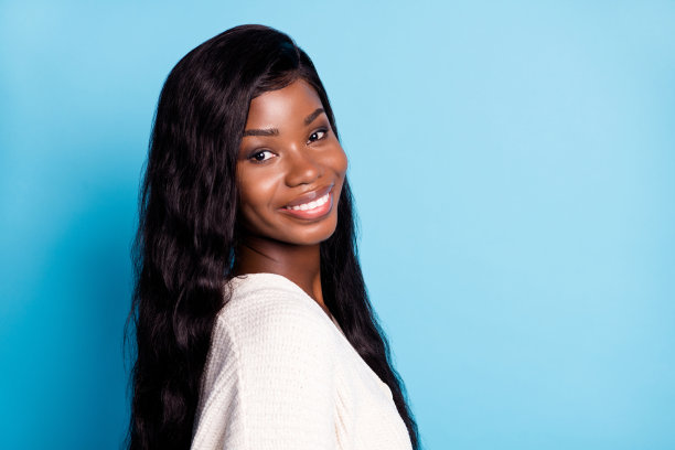侧面肖像照片：一位非裔美国年轻女性，面带微笑，心情愉快，背景为柔和的蓝色。图片下载