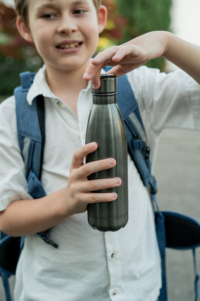 背着书包的小男孩正在打开一个铁水瓶。开学季。学习。图片下载