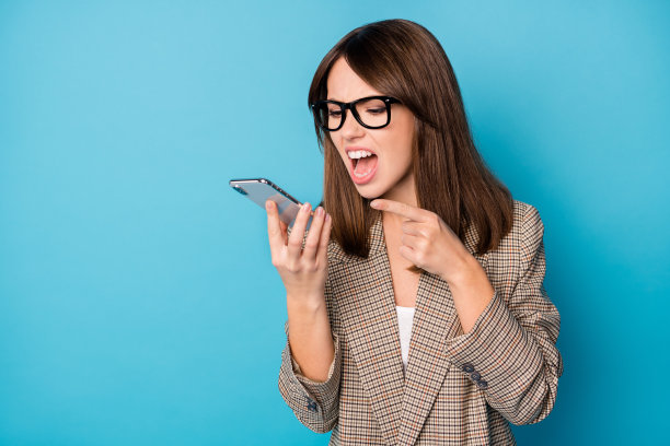 愤怒的女人在鲜艳的蓝色背景下，手持手机用一只手指着并大声尖叫的照片肖像图片下载