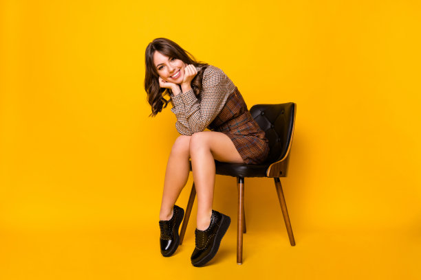 穿着格子校服的女学生坐在椅子上，背景为明亮的黄色，展示全身照片。图片下载