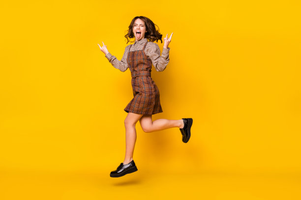 身穿重金属风格校服的女学生在明亮的黄色背景下跳跃并吐舌头的全身照片图片下载