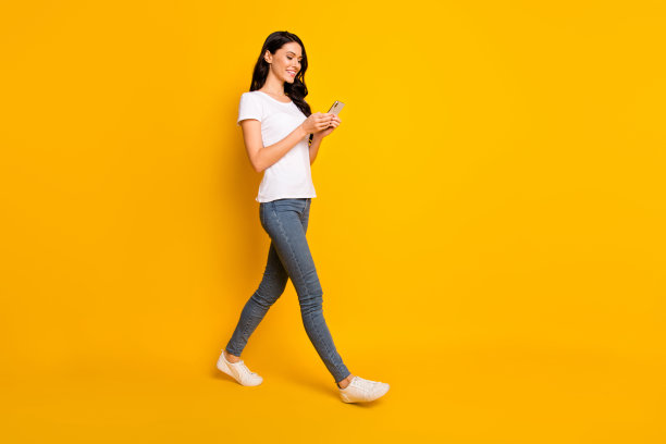 漂亮女孩的全身侧面照片，空旷的空间中手持智能手机，红色信息，背景为黄色。图片下载