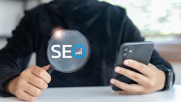 特写手握放大镜，放大镜上有SEO图标和智能手机，搜索引擎优化、数字营销、内容策略和在线可见性的概念。图片下载