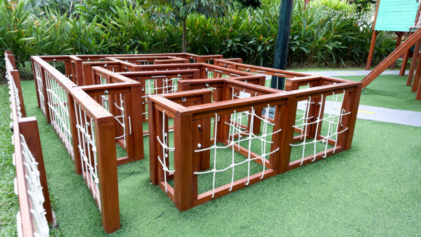 这张图片展示了一个棕色木制迷宫结构，配有白色绳网，置于明亮的绿色人造草坪上。这是一个引人入胜的游乐场设施，旨在让孩子们探索和玩乐。图片下载