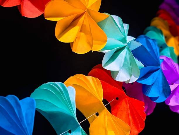 横向照片，展示了两条色彩鲜艳的纸花环悬挂在黑色背景上的绳子上。图片下载