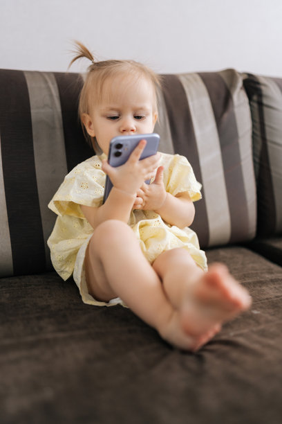 专注的幼儿女孩在家中舒适地坐着，使用智能手机屏幕探索数字内容的竖拍照片图片下载